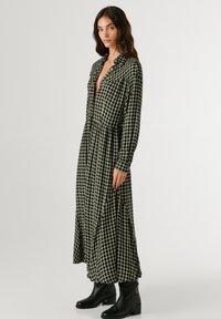 Μακρυμάνικο, πουκάμισο φόρεμα σε σκούρο πράσινο και κρεμ καρ�ό σχέδιο, με στενή μέση και πλισέ φούστα, συνδυασμένο με μαύρες μποτάκια μέχρι τον αστράγαλο.