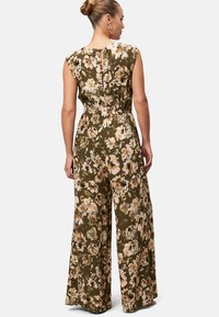 Combinaison fleurie en tissu vert olive. Présente des jambes larges, un design sans manches et un dos ouvert avec un détail en forme de clé. Fleurs dans des teintes de crème et de noir.