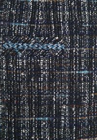 Tessuto dalle texture in blu navy con macchie multicolori. Contiene una piccola tasca con dettagli intrecciati. Tessitura complessiva con un motivo variato in spessore.