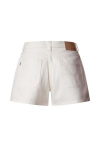 Valged teksapüksid, millel on kaks taga taskut, vööaasad ja pruun nahast brändimärk vöökohal.