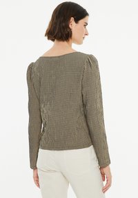 Top de manga larga a cuadros en blanco y negro con cuello redondo y hombros abullonados, que presenta una silueta ajustada y un tejido texturizado.