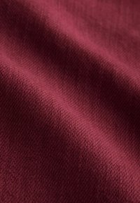 Burgundy textured fabric with visible fine weave, showcasing a smooth feel and soft appearance in a rich, deep color.