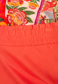 Tecido com padrão floral em tons de rosa, vermelho e verde, combinado com uma cintura em coral com elástico franzido para um ajuste confortável.
