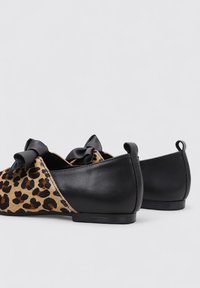 Bailarinas de estampado de leopardo con parte trasera de cuero negro, dos lazos de satén negro en la parte delantera y una suela baja y plana.