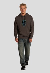 Felpa con cappuccio grigia scura con una grafica colorata di un personaggio dei cartoni animati sul davanti, abbinata a jeans larghi di un blu chiaro e scarpe da ginnastica nere.