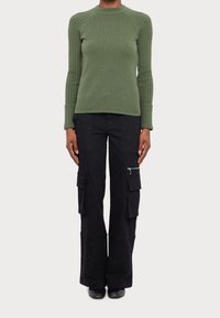 Haut vert à manches longues en tricot avec texture côtelée et silhouette ajustée, associé à un pantalon cargo noir avec poches zippées.