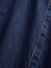 Dunkelblaue Denim-Stoff mit glatter Textur, versehen mit kontrastierendem gelben Nähten entlang der Naht für zusätzliche Details.