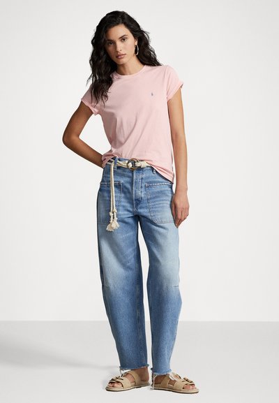 Camiseta de algodón rosa claro con mangas enrolladas, combinada con jeans de pierna ancha azul claro con bolsillos de parche y un cinturón de cuerda. Sandalias beige.