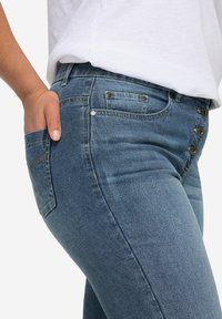 Jeans de mezclilla azul con un diseño de cintura alta, cinco bolsillos y una cremallera lateral. Textura suave con un ligero desgastado.