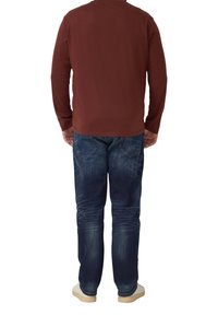 Bordowa koszula z długim rękawem i ciemnoniebieskie dżinsy z wyblakłym wzorem, widziane od tyłu, w połączeniu z jasnymi butami.