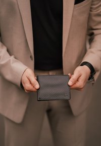 Black leather wallet with textured surface, bi-fold design, and stitched edges. Features a subtle logo on the lower corner.