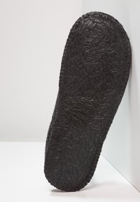 Zwarte rubberen zool met een gestructureerd bladpatroon, gebogen vorm en een geribbelde rand, gekanteld tegen een lichte achtergrond.