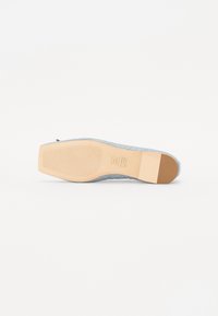 Chaussure bleu clair avec une tige texturée et une semelle extérieure en caoutchouc beige contrastante. Présente un bord lisse et un détail de logo en relief subtil.