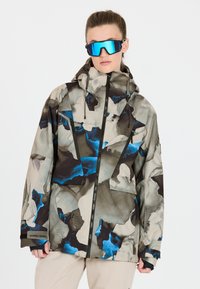 Winterjacke im Tarnmuster mit einer Mischung aus Beige-, Schwarz- und Blautönen, verstellbarer Kapuze und Reißverschlusstaschen.