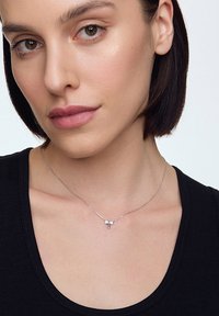 Srebrny naszyjnik z delikatnym łańcuszkiem, ozdobiony małym uroczym motylkiem oraz trzema maleńkimi kamieniami szlachetnymi. Modelka nosi czarną bluzkę.