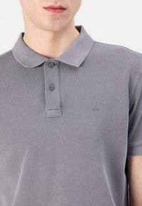 Polo gris hecho de algodón texturizado, con cuello, tapeta de dos botones y un logo sutil en el pecho.