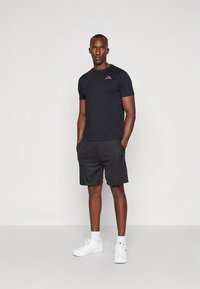 Must lühikeste varrukatega T-särk, millel on rinnal logo, kombineeritud tumedatehallide lühikestega. Kandatud valgete tossude ja sokkidega. Lihtne sportlik disain.