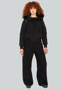 Sort cropped jakke med en pelsforret huood, et par løse sorte bukser og sorte sneakers. Glat tekstur med to forreste lommer.