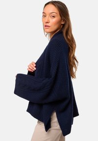 Pull en tricot large bleu marine avec un motif texturé, des manches larges et des accents en tricot torsadé le long des poignets.