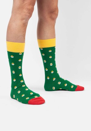 Grüne Baumwollsocken mit gelben Rippabschlüssen und roten Zehen, die ein Muster aus weißen Eiern mit gelben Eigelben zeigen.