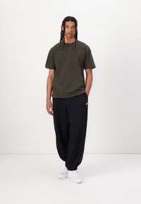 Tricou scurt, de culoare verde măsliniu închis, cu un croi relaxat, asortat cu pantaloni scurți negri din bumbac și încălțăminte albă. Design simplu, fără modele.