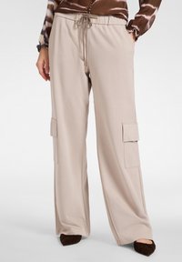 Beige cargobroek met wijde pijpen, een elastische taille, trekkoord en twee zijzakken. Zachte stof met een gladde textuur.