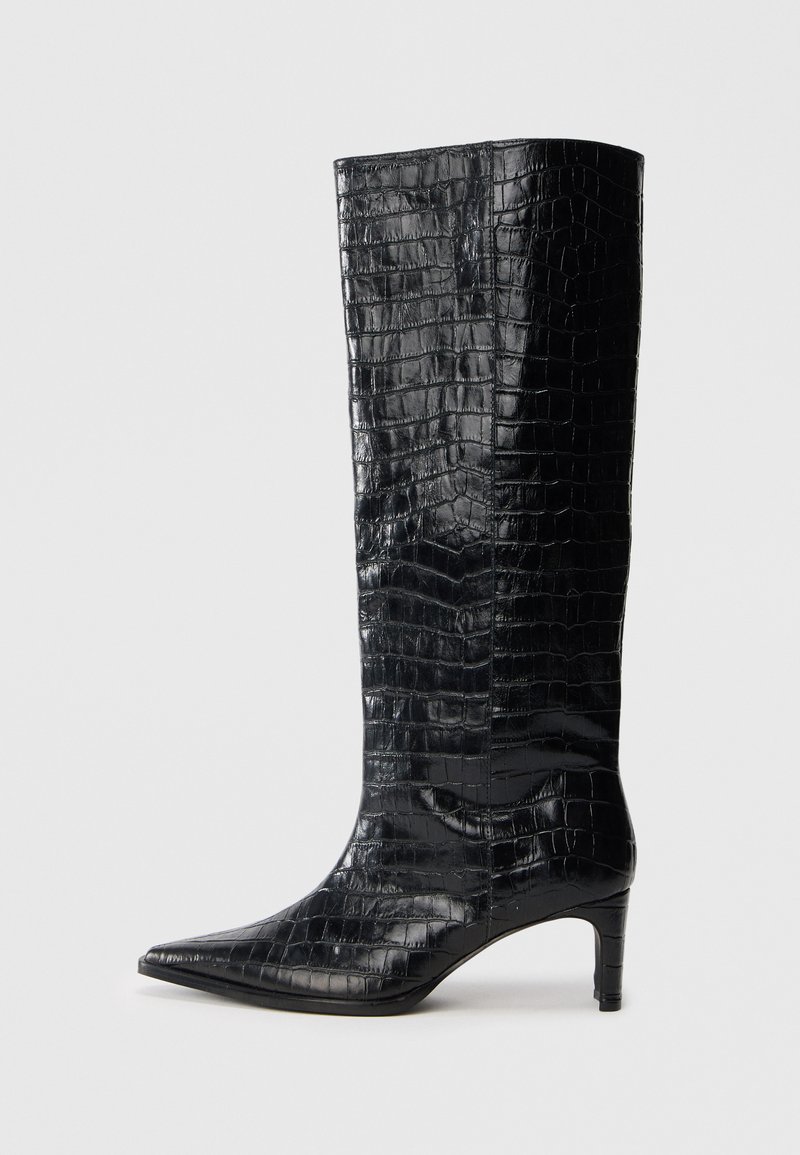 Bottes noires montantes, avec une texture brillante à motif crocodile, bout pointu et talon effilé. Matériau synthétique lisse.