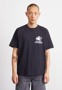 Schwarzes Baumwoll-T-Shirt mit einem weißen Grafikdruck mit dem Text „LOKALE DIENSTLEISTUNGEN“ auf der Brust. Bequemer Schnitt, kurze Ärmel und Rundhalsausschnitt.