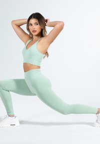 Lichtgroene geribbelde sportbh en bijpassende high-waisted legging. De outfit heeft een aansluitend ontwerp, een soepele textuur en minimale branding.