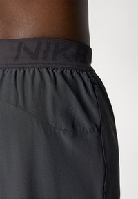 Fekete sportnadrág légáteresztő anyagból, perforált mintázattal és elasztikus derékkal, amelyen a "NIKE" márkaneve szerepel.