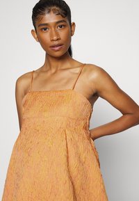 Vestido de verão laranja amarrotado com alças finas, apresentando um ajuste solto e uma textura sutil. O tecido tem um leve brilho e uma bainha em camadas.