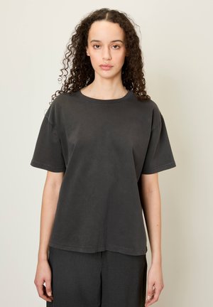 Un t-shirt noir à manches courtes en tissu doux, avec un col rond et une coupe décontractée, associé à un pantalon gris foncé.