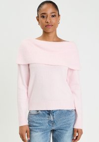 Pull léger rose à épaules dénudées avec texture côtelée au niveau de l'encolure, manches longues et ourlet ajusté côtelé, associé à un jean bleu.