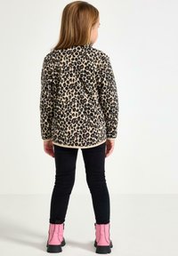 Leopardmønstret fleecejakke med cremegul baggrund og rund kant. Sorte slim-fit bukser og pink ankelstøvler med lynlåse.
