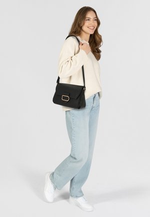 Zwarte leren handtas met gouden hardware, gestructureerde vorm, klepvergrendeling en verstelbare schouderband. Draag met lichtblauwe jeans en witte sneakers.