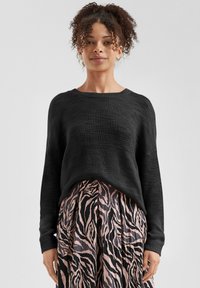 Zwarte gebreide trui met een losse pasvorm, wijde halslijn en textuurstof, gecombineerd met een geplooide rok met een roze en zwart zebra-patroon.