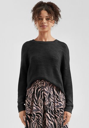 Schwarzer, gestrickter Pullover mit lockerer Passform, weitem Ausschnitt und strukturiertem Stoff, kombiniert mit einem plissierten Rock im Zebra-Muster in Pink und Schwarz.