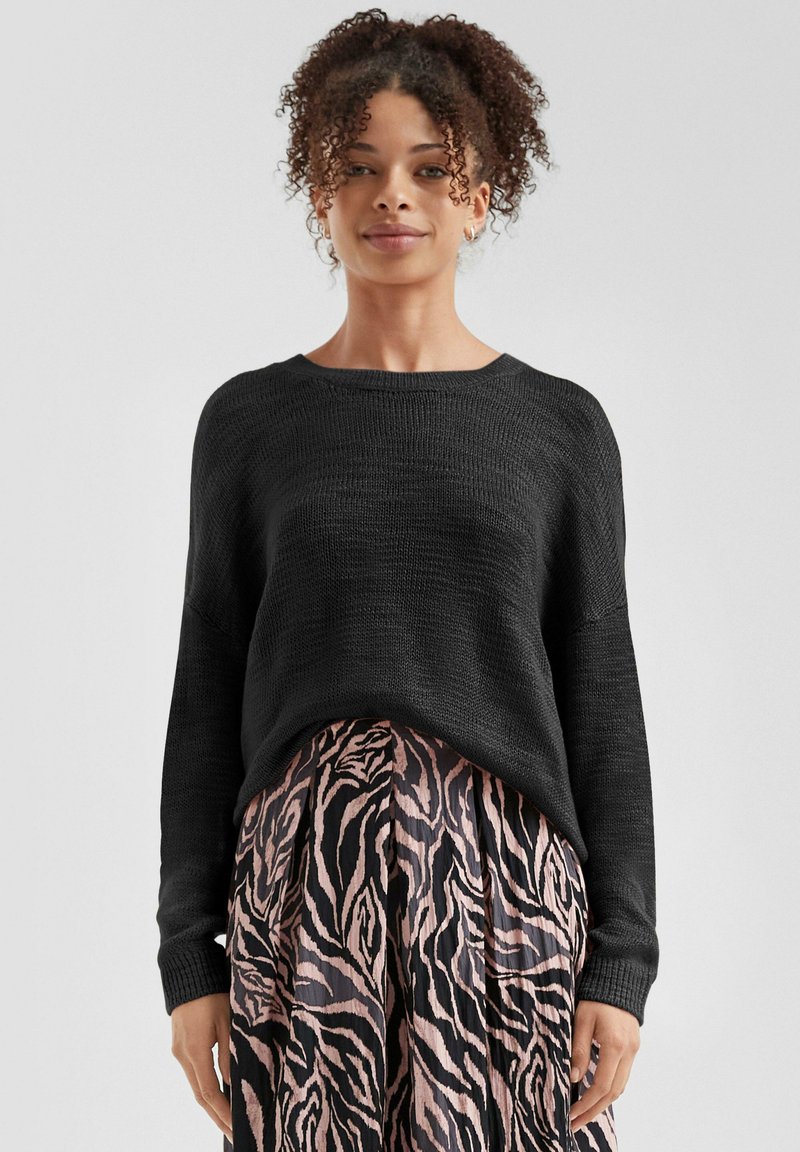 Zwarte gebreide trui met een losse pasvorm, wijde halslijn en textuurstof, gecombineerd met een geplooide rok met een roze en zwart zebra-patroon.