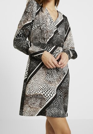 Robe portefeuille noir et blanc avec un motif serpent et des rayures diagonales, manches longues et décolleté en V. Texture de tissu douce.