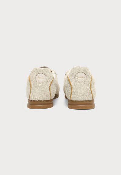 Paire de chaussures en daim beige vues de dos avec semelles marron et détails de couture sur fond blanc uni.