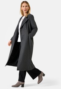 Grijze wolmix overjas met een dubbel gebreide ontwerp, brede revers, en zijzakken, gecombineerd met donkere broeken en grijze haklaarzen.