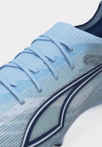 Light blue athletic shoe with textured knit upper, matching laces, and a dark blue outlined logo on the side panel.