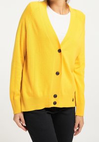 Žlutý cardigan s výstřihem do V, dlouhými rukávy a ribbovaným lemem. Obsahuje pět černých knoflíků a strukturovaný pletený materiál s jemnými detaily.