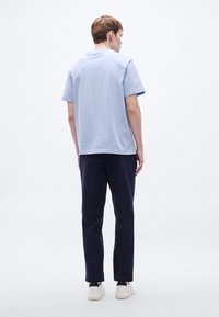 Jasnoniebieski bawełniany t-shirt z krótkimi rękawami, zestawiony z granatowymi spodniami. Model nosi białe trampki, ukazany od tyłu.
