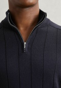 Ciemnogranatowy sweter z połową zamka, z pionowymi prążkami, dopasowanym kołnierzem i srebrnym detalem zamka.