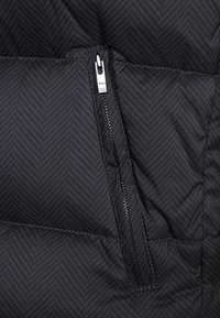 Schwarzer gesteppter Stoff mit Fischgrätenmuster; verfügt über ein silbernes Reißverschlussdetail auf der linken Seite, das ein elegantes und strukturiertes Erscheinungsbild schafft.