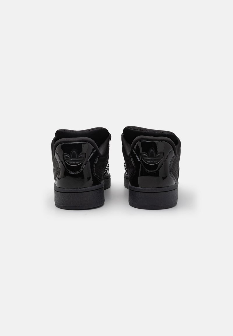 Zapatillas negras con un acabado de charol brillante, que cuentan con un talón texturizado, un cuello acolchado y un detalle de logo en relieve en la parte trasera.