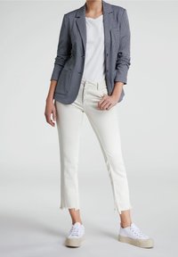 Blazer à carreaux bleu marine et blanc, T-shirt blanc, jean blanc court avec ourlet effiloché, et baskets blanches à semelles beiges.