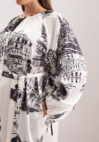 Langärmliges Kleid aus leichtem, weißem Stoff mit schwarzem architektonischem Druck. Mit gerafftem Ausschnitt und Taillengürtel. Ausgestellte Ärmel, seitliche Taschen.