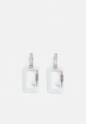 Boucles d'oreilles créoles rectangulaires blanches avec fermoirs argentés ornés de petits cristaux et détail toggle argenté étiqueté "Guess."